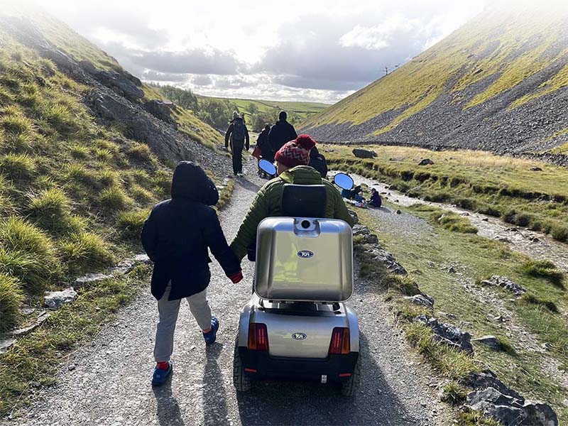 Group of people including an electric wheelchair user heading up a trail