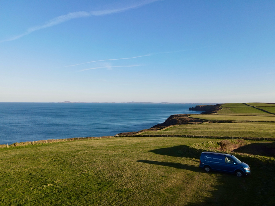 A blue van parked on a grassy hill with the sea behind