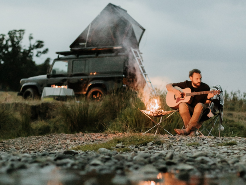 man playing guitar in front of camp fire