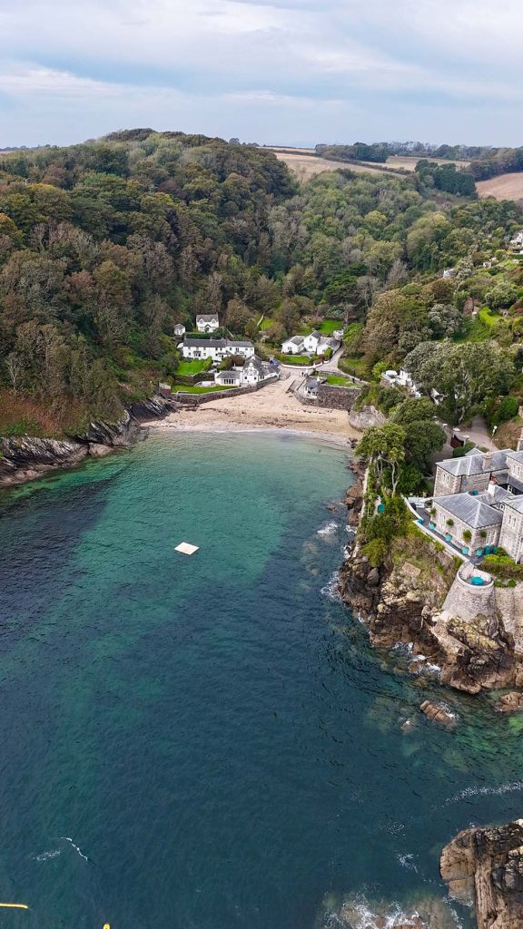 Aerial view of a coastal area featuring a sandy beach, lush greenery, and residential homes situated on the hillside.