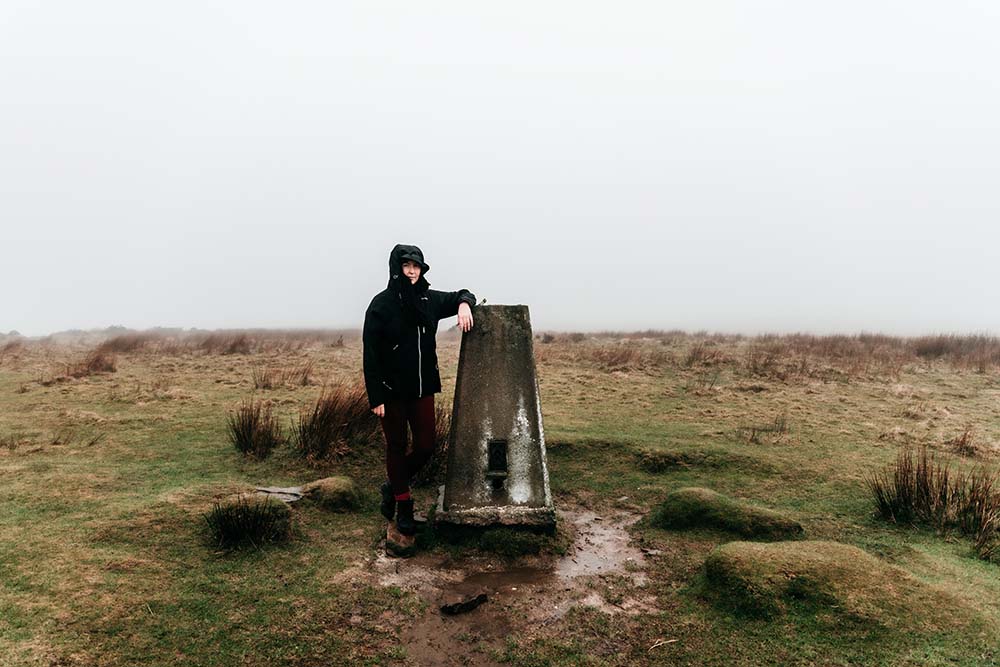 Person standing next to a Trig point