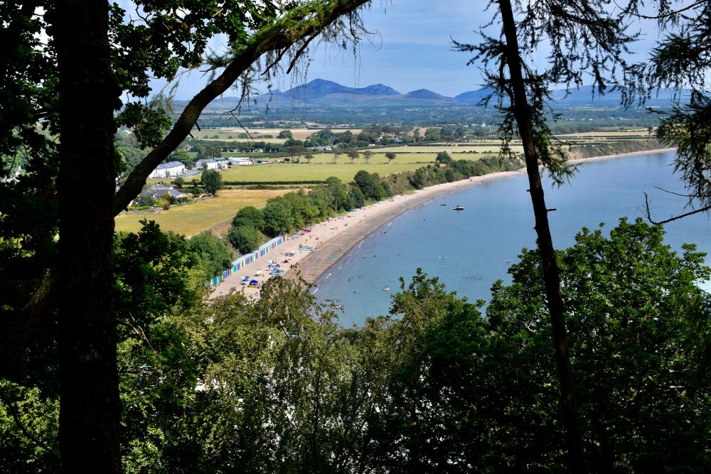 Peering through trees at the mountains and the beach huts from Llanbedrog Beach Mountain