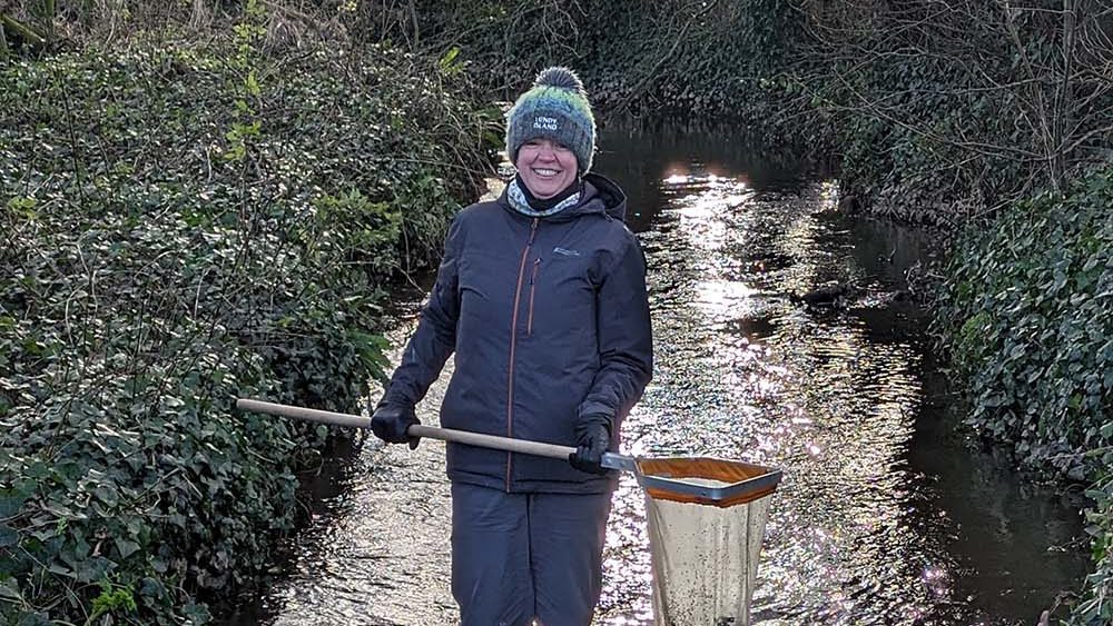 A woman in a stream measuring water pollution with a net