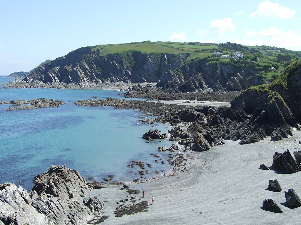 A scenic beach view featuring rocky cliffs and calm turquoise waters under a clear blue sky.