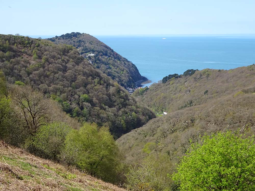 A scenic view of a coastal landscape featuring lush green hills and a blue sea in the distance, with a small village nestled in the valley.