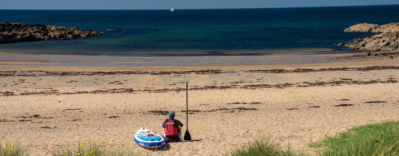 a lone figure with a paddle board sat on a beautiful british beach