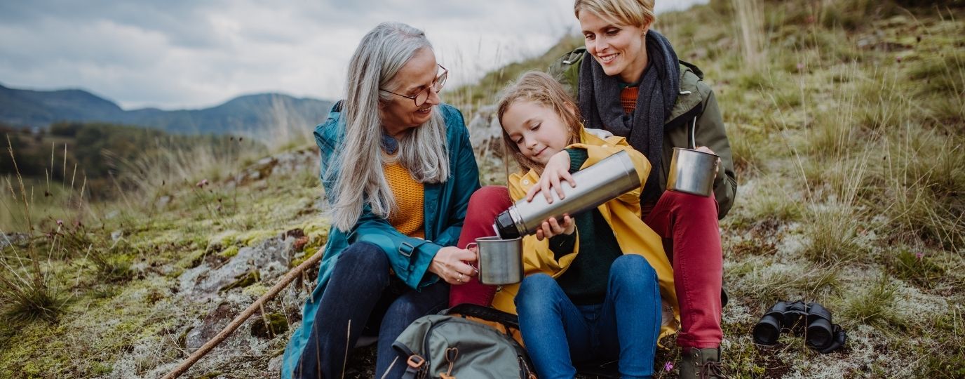 A grandmother and her daughter and grandaughter enjoying a flask of hot drink on a walk