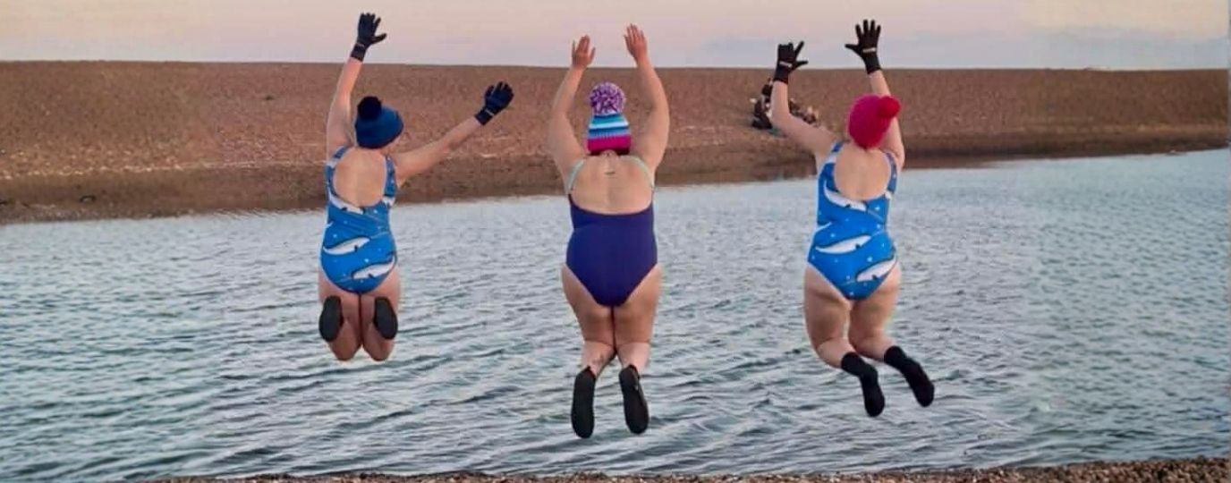 3 women leaping on a beach in swimming costumes