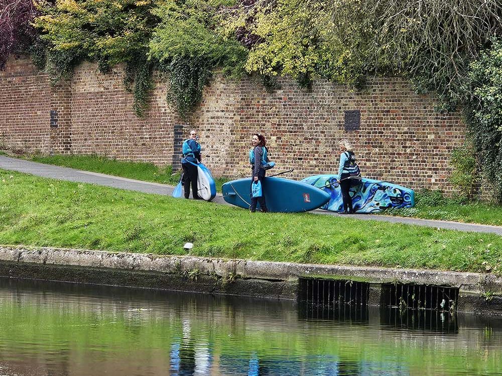 carrying paddleboards along a grassy river bank