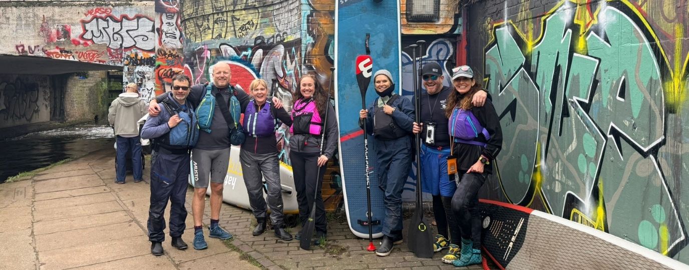Anu Aladin with friends and her paddleboard by a canal bridge covered in graffiti