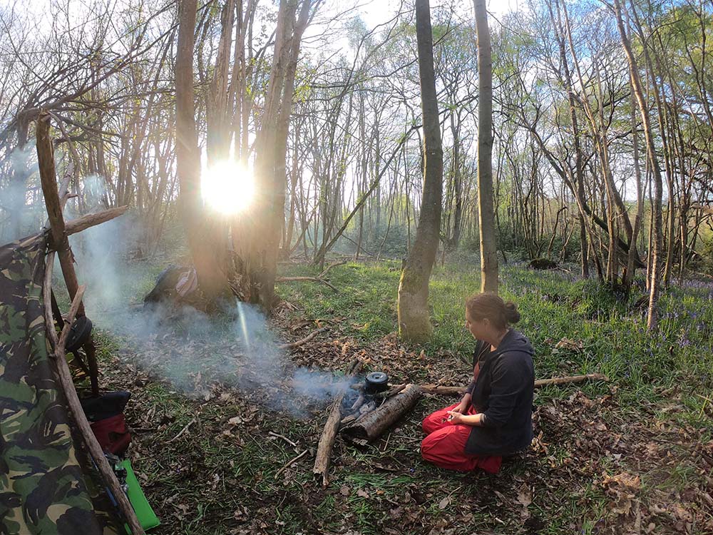 a woman kneeling by a camp fire