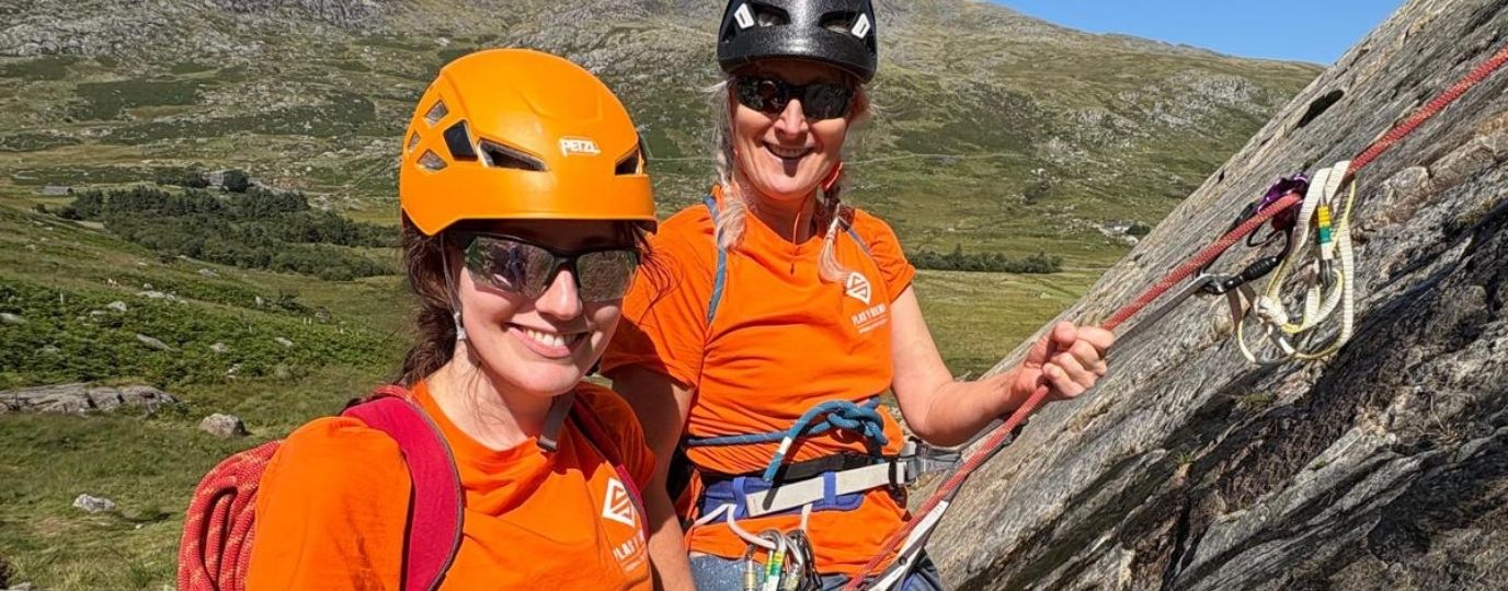 two women wearing orange rock climbing and smiling
