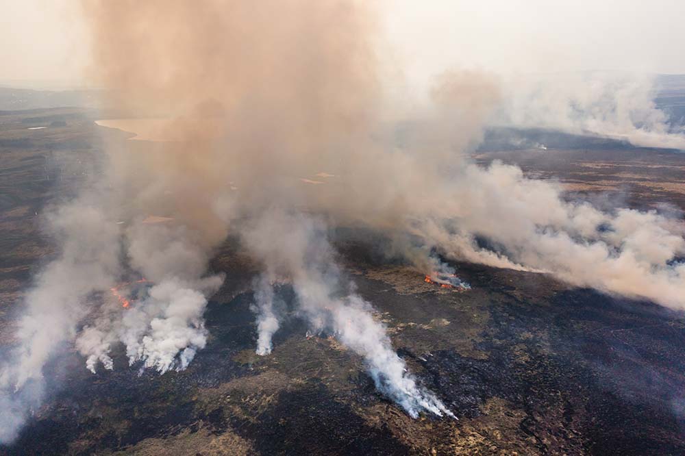 Aerial view of smoke and flames from a large grassfire on moorland in South Wales, UK (Llangynidr Moors, Wales)